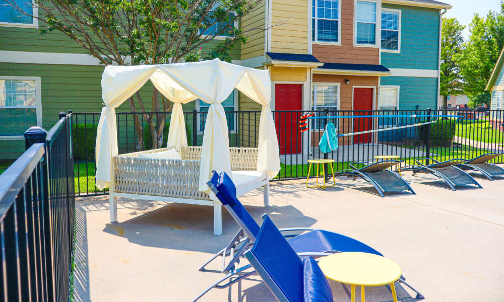 A white canopy daybed and blue lounge chairs in the pool area at Alameda Pointe in Norman, Oklahoma