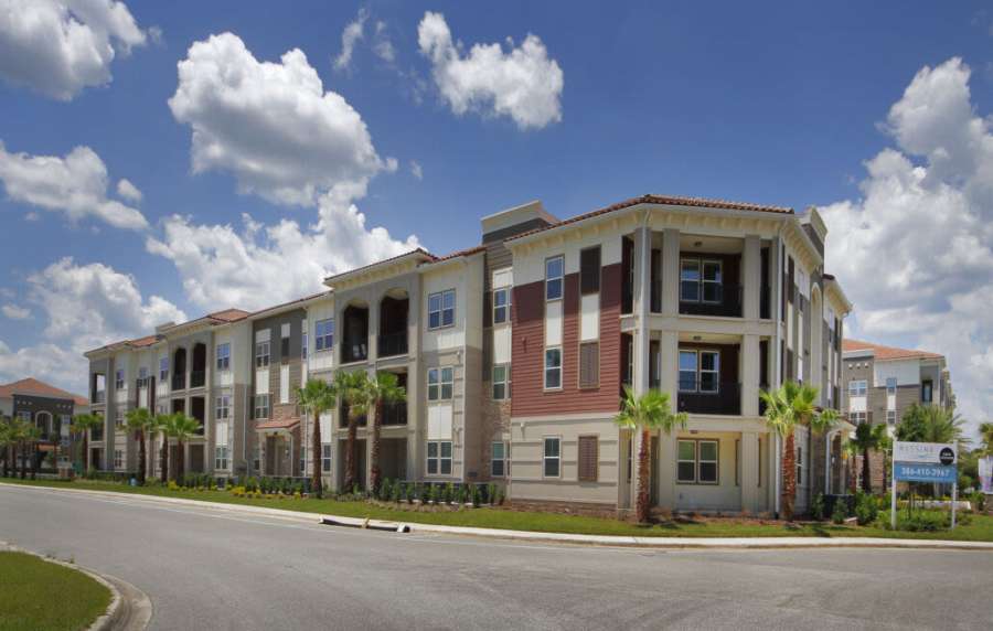 Modern apartment complex with palm trees and clear blue skies at Messina Luxury Apartments in New Smyrna Beach, Florida