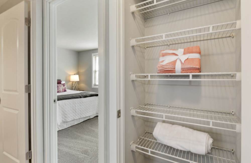 Storage closet with neatly folded towels and a view into a cozy bedroom with carpeted flooring at Fairway Ridge in Baltimore, Maryland