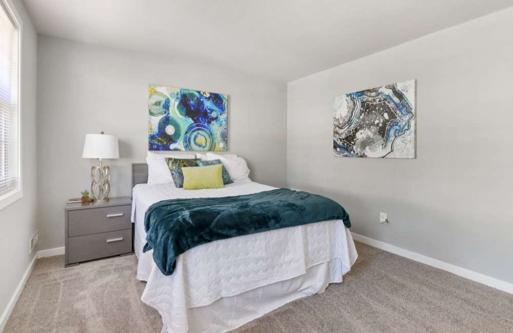 Cozy bedroom with plush carpet, modern artwork, and bedside lamp on nightstand at Fairway Ridge in Baltimore, Maryland