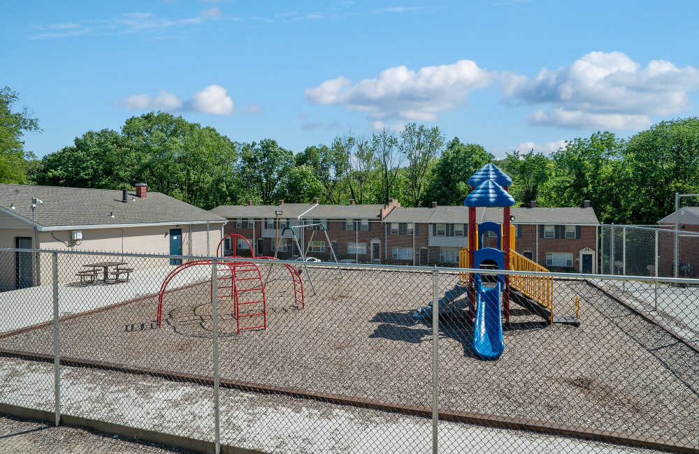 Playground area with swings and slide, surrounded by a fenced yard and picnic tables at Fairway Ridge in Baltimore, Maryland