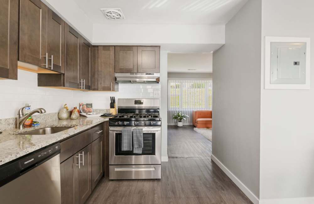 Modern kitchen with granite countertops, stainless steel appliances, and wood-style flooring leading to living area at Fairway Ridge in Baltimore, Maryland