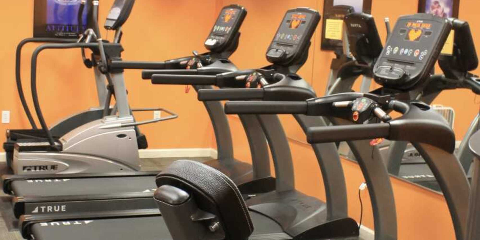 Fitness center with modern treadmills and elliptical machines against an orange wall at Castle Ridge Apartments in Pittsburgh, Pennsylvania