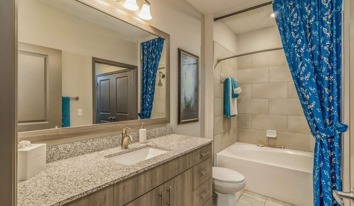 Bright bathroom with vanity light, mirror, sink, commode and bathtub at The Addison on Millenia in Orlando, Florida