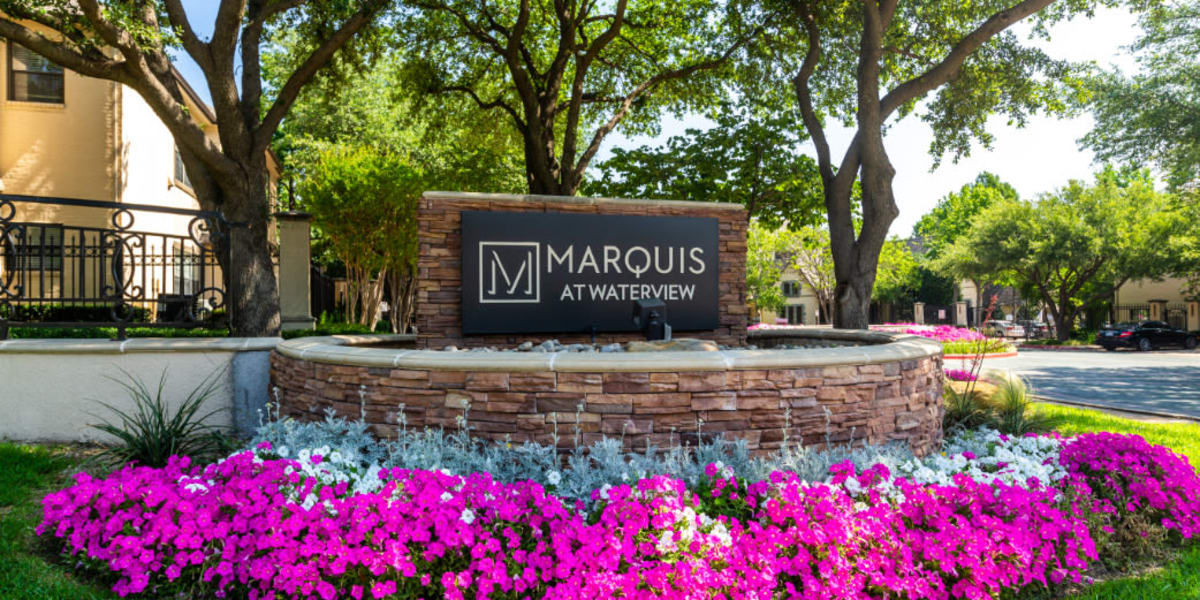 Property stone sign surrounded by colorful flowers and plants at Marquis at Waterview in Richardson, Texas