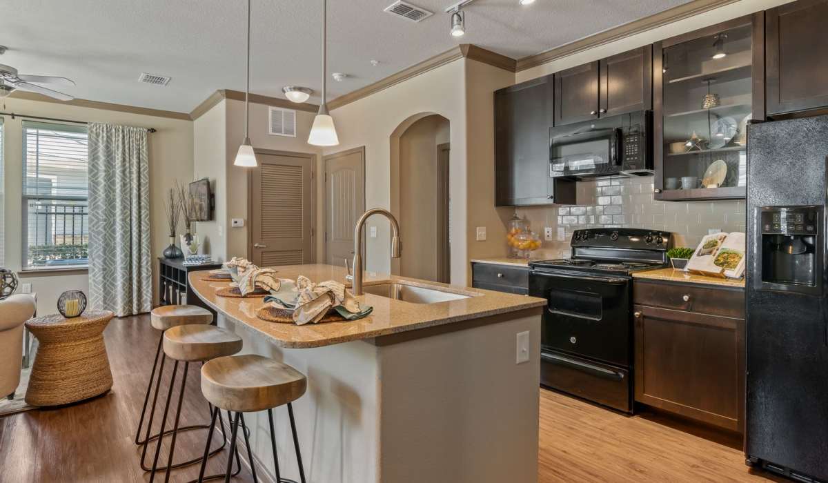 Modern kitchen with black appliances, storage spaces, island countertop and barstool at The Crosby at Towne Center in Sanford, Florida