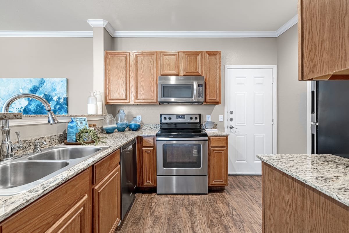 Modern style kitchen with wood cabinets, wood flooring, and granite countertops at Marquis at The Cascades in Tyler, Texas