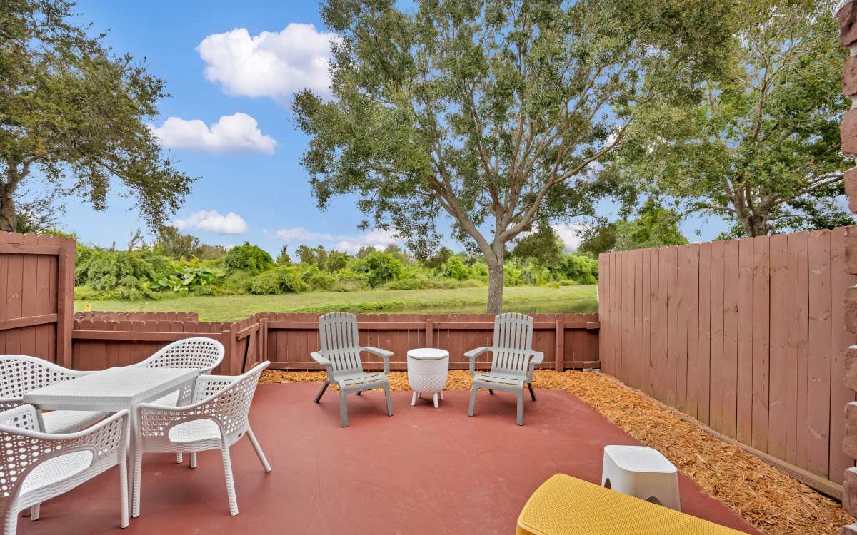 Outdoor patio featuring seating area with chairs and table, surrounded by a fenced yard and greenery at Carlton Arms Of Winter Haven in Winter Haven, Florida
