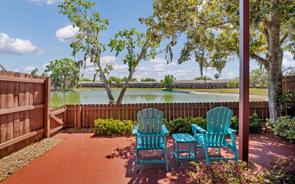 Private fenced patio with outdoor seating, overlooking a scenic lake with surrounding trees at Carlton Arms Of Magnolia Valley in New Port Richey, Florida