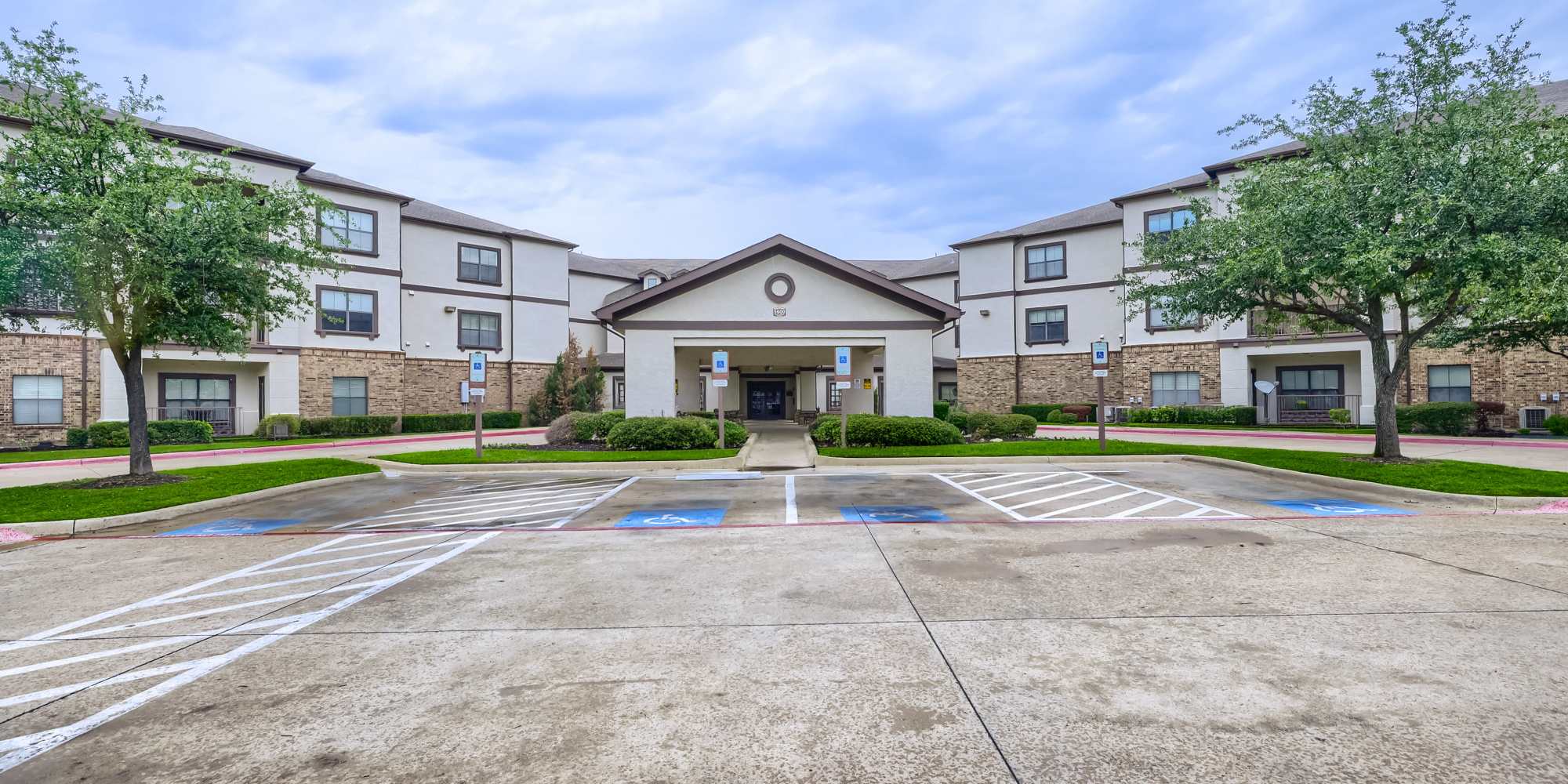 Modern apartment community with well-maintained landscaping and accessible parking spaces at Lindbergh Parc Senior Apartments in Fort Worth, Texas