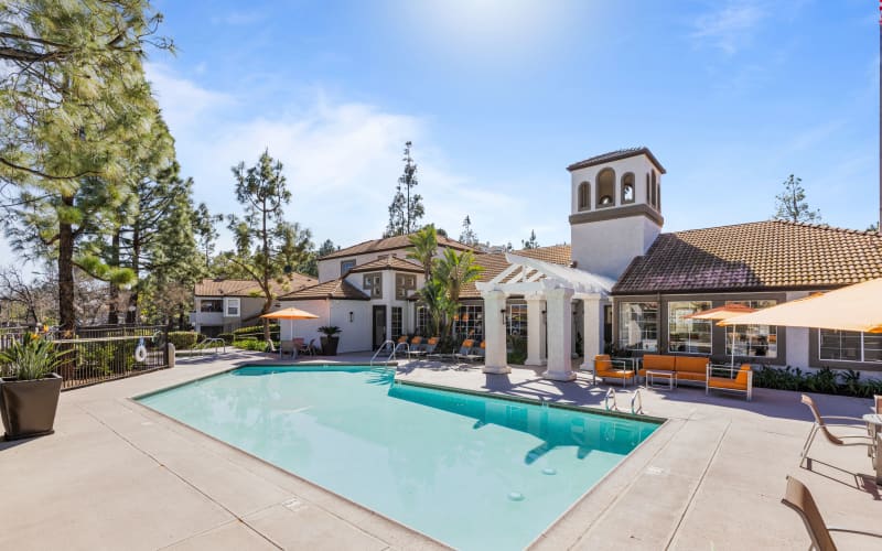 Large swimming pool with lounge chairs and umbrellas at Sierra Del Oro Apartments in Corona, California