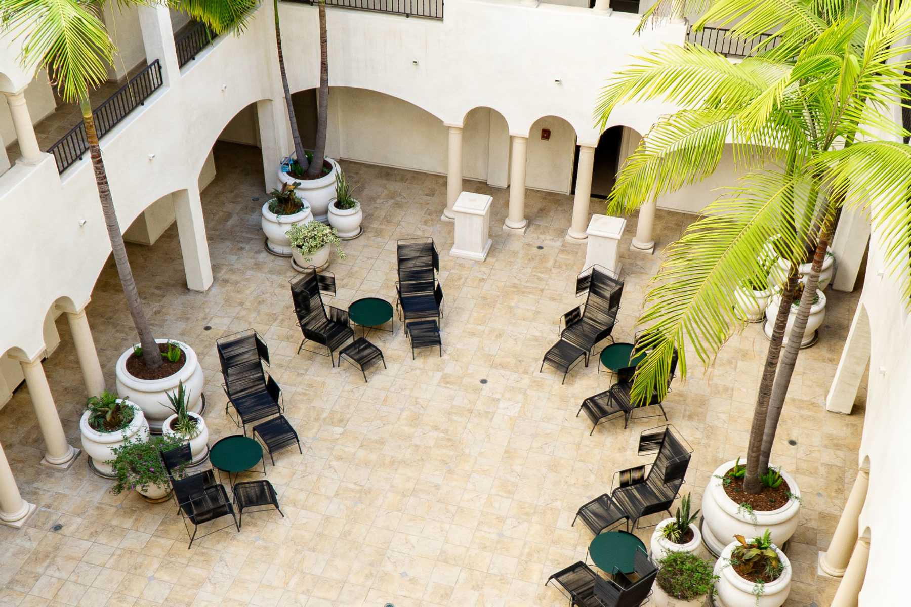Courtyard with tiered fountain, black chairs, green tables, palm trees, and arched walkways at Luxe Villas in Brentwood, California