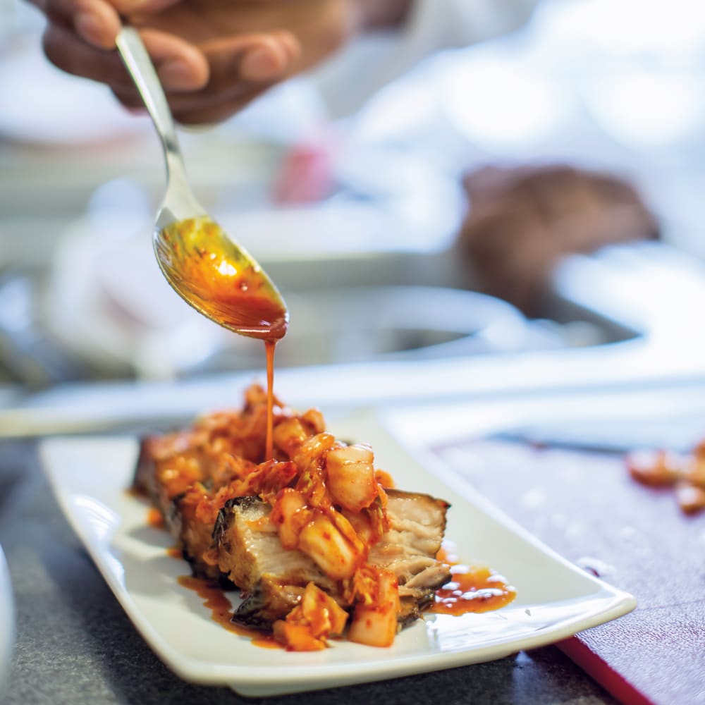 Chef at Anthology of Farmington Hills in Farmington Hills, Michigan dripping sauce onto a meal