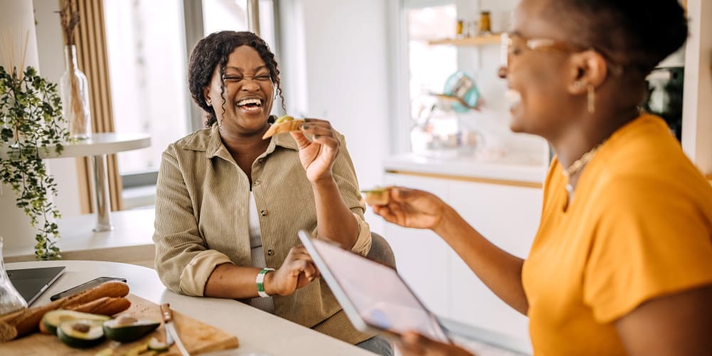 Two women laughing and eating in an apartment at The Pines at Peachtree in Columbus, Georgia