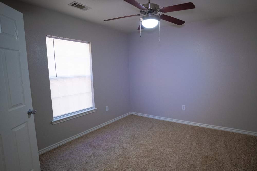 Unfurnished bedroom with ceiling fan, carpet flooring and large window at Timber Village II in Marshall, Texas