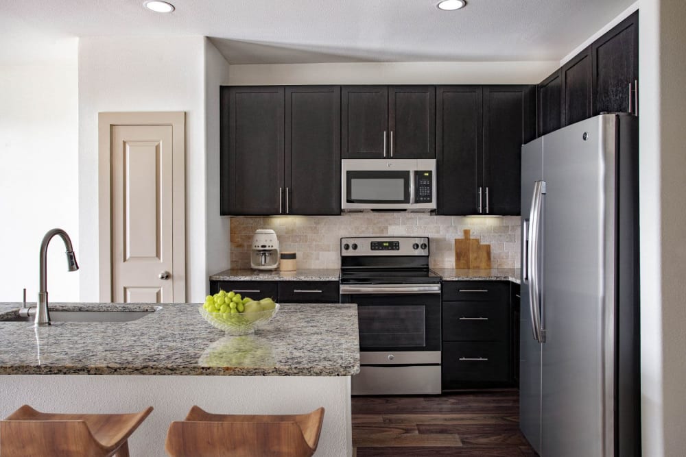 Granite counter island with bar stool chairs and stainless steel appliances in kitchen at Olympus Falcon Landing in Katy, Texas