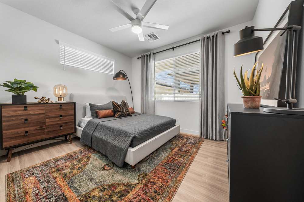 Specious bedroom with cozy bed, side lamp, wood-style flooring and a large window at Obsidian at South Mountain in Phoenix, Arizona