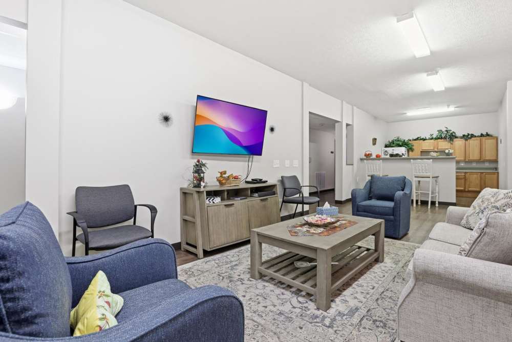 Cozy living room with blue sofas, coffee table, and kitchen in background with wood cabinetry at Norwood Greene Senior Living in Marietta, Ohio
