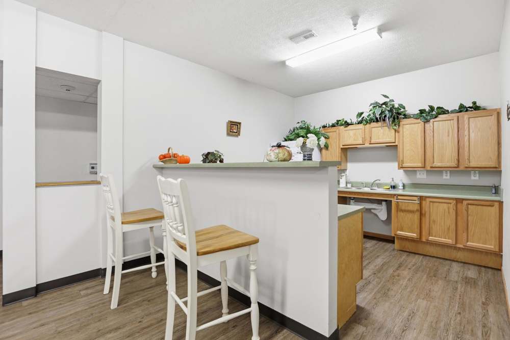 Bright kitchen with wood-style flooring, wooden cabinets, and bar seating with two chairs at Norwood Greene Senior Living in Marietta, Ohio