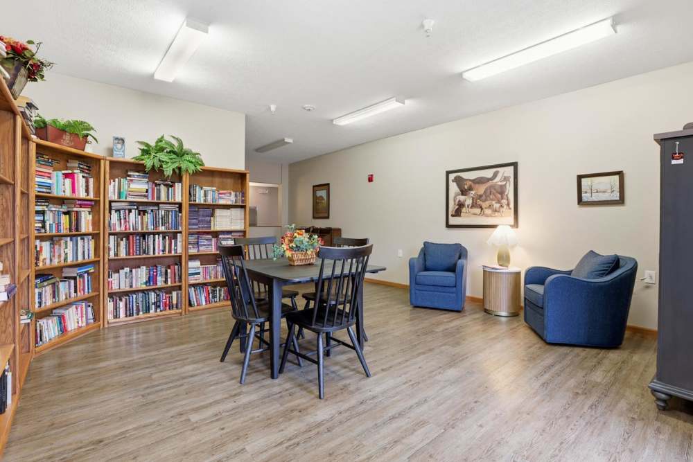 Cozy community lounge with wood-style flooring, bookshelves, and a round dining table with chairs at Norwood Greene Senior Living in Marietta, Ohio