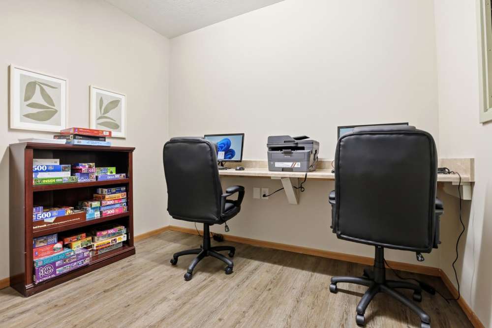 Home office with two ergonomic chairs, desk, printer, and bookshelf filled with board games at Norwood Greene Senior Living in Marietta, Ohio