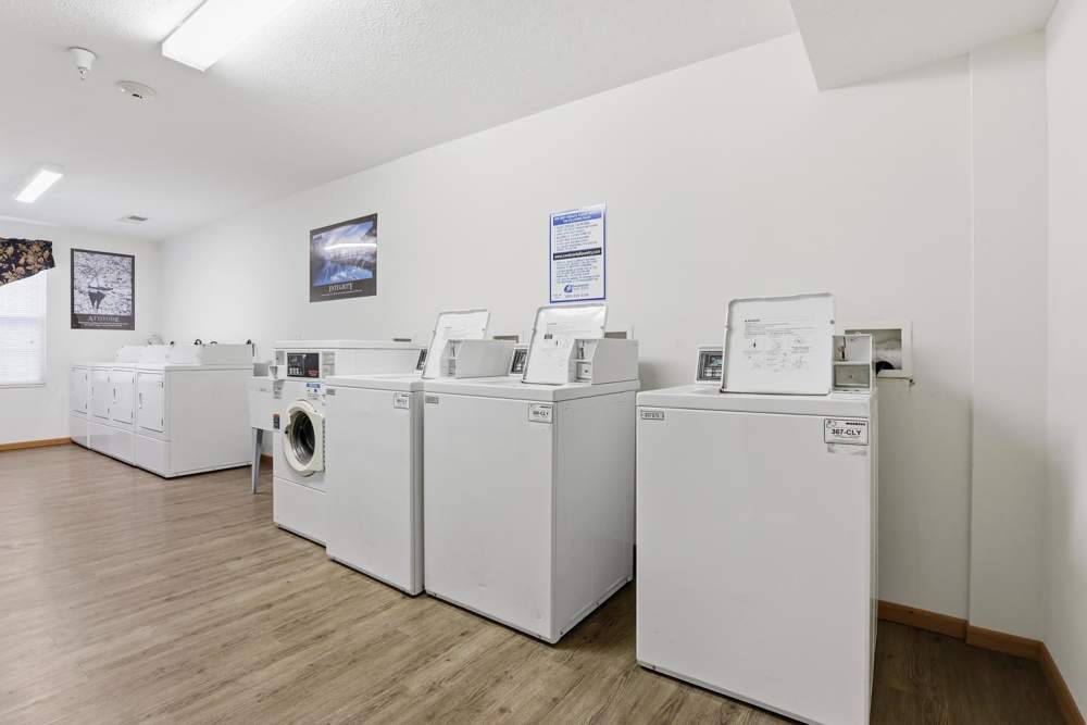 Laundry room with multiple white machines and wood-style flooring, bright lighting, and decorative wall art at Norwood Greene Senior Living in Marietta, Ohio