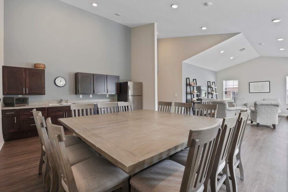 Bright community room with wood-style flooring, large dining table, modern kitchen, and cozy seating area at Wheatland Crossing II in Columbus, Ohio