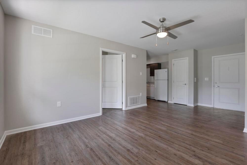 Spacious living area with wood-style flooring and ceiling fan, leads to kitchen with white appliances at Wheatland Crossing II in Columbus, Ohio