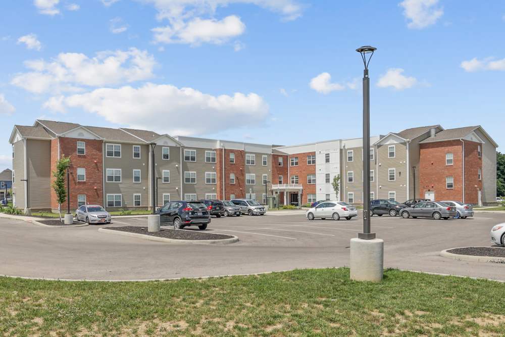 Apartment community exterior with landscaped lawn, parking area, and three-story buildings under a blue sky at Wheatland Crossing II in Columbus, Ohio