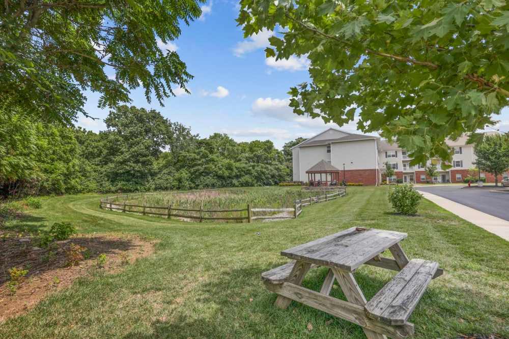 Picnic table in green space near a pond with wooden fencing and trees in the background at Wheatland Crossing II in Columbus, Ohio