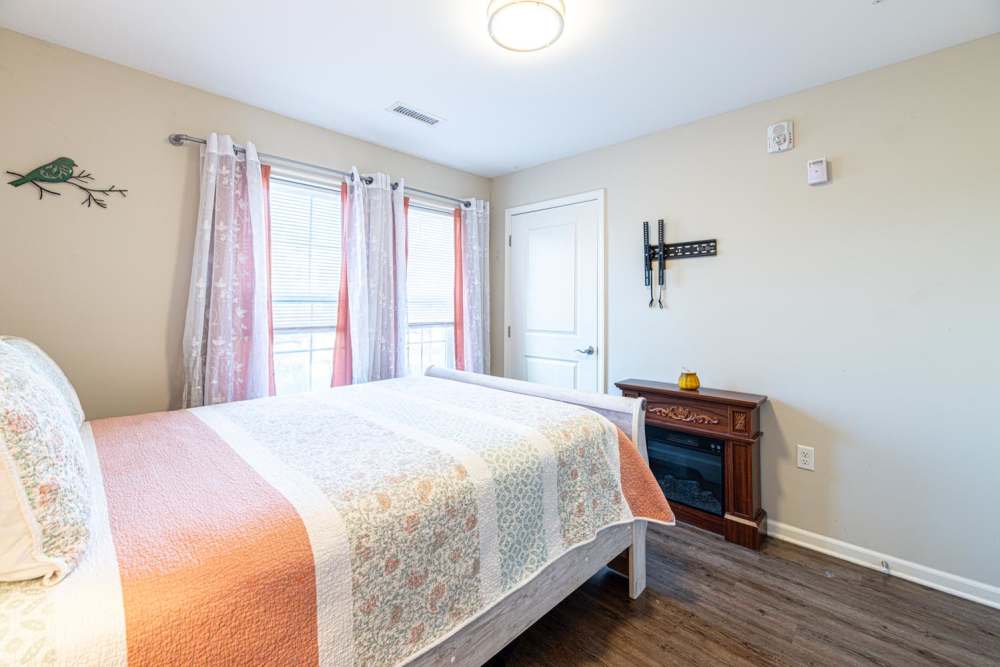 Cozy bedroom with wood-style flooring, large windows, and decorative curtains at White Oak Crossing in Knoxville, Tennessee