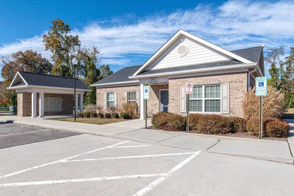 Gated entrance with brick building and landscaped shrubs under clear blue sky at White Oak Crossing in Knoxville, Tennessee