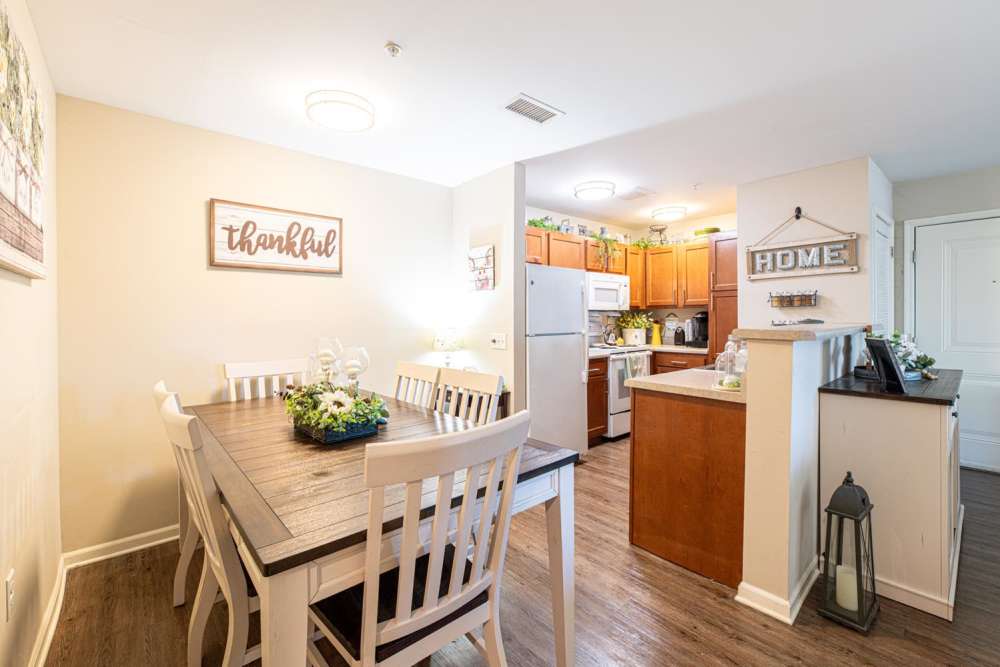 Open layout kitchen with stainless steel appliances and granite countertops, dining area with wood-style flooring and table centerpiece at White Oak Crossing in Knoxville, Tennessee