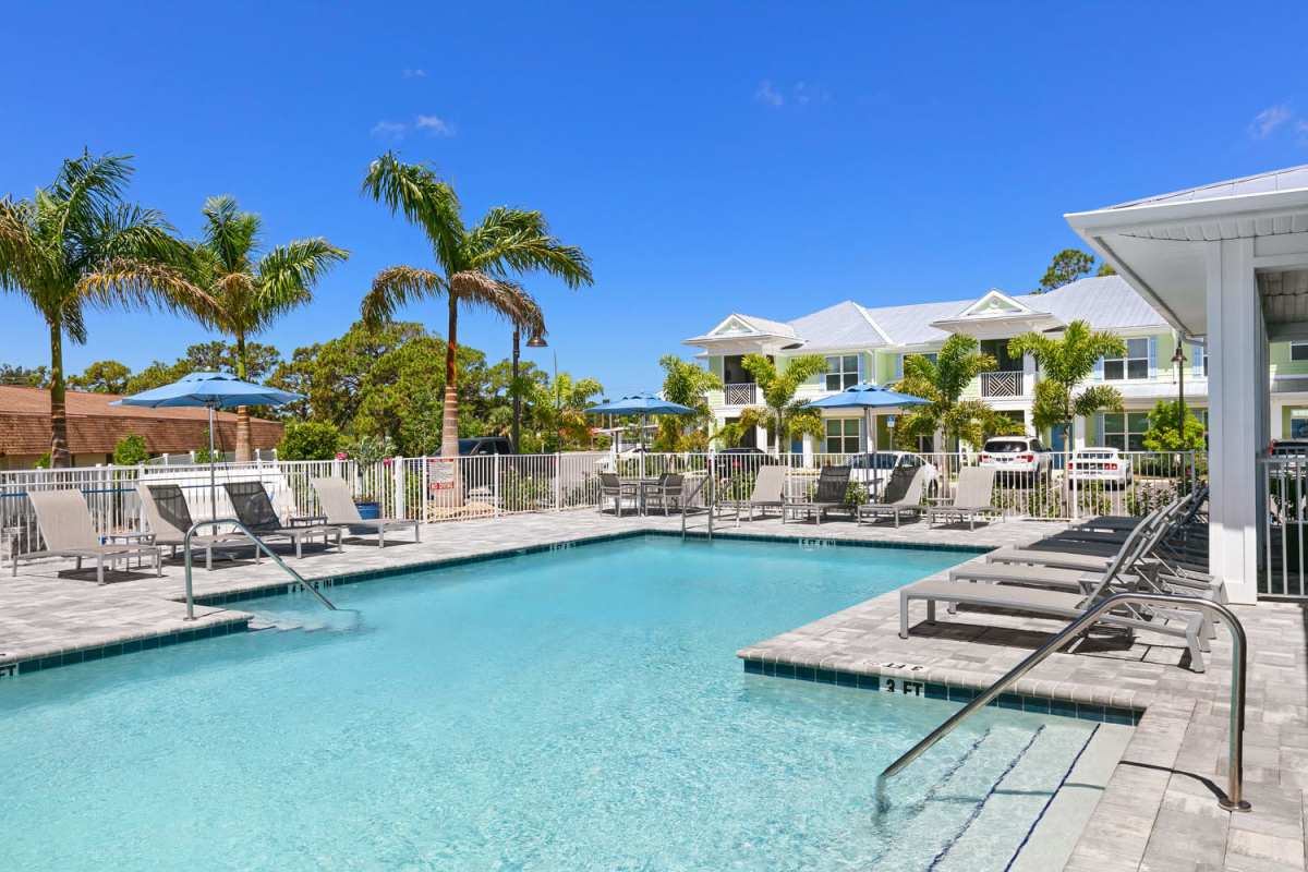 Woman putting her feet in the pool and looking at her phone at Lemon Bay Apartments in Englewood, Florida