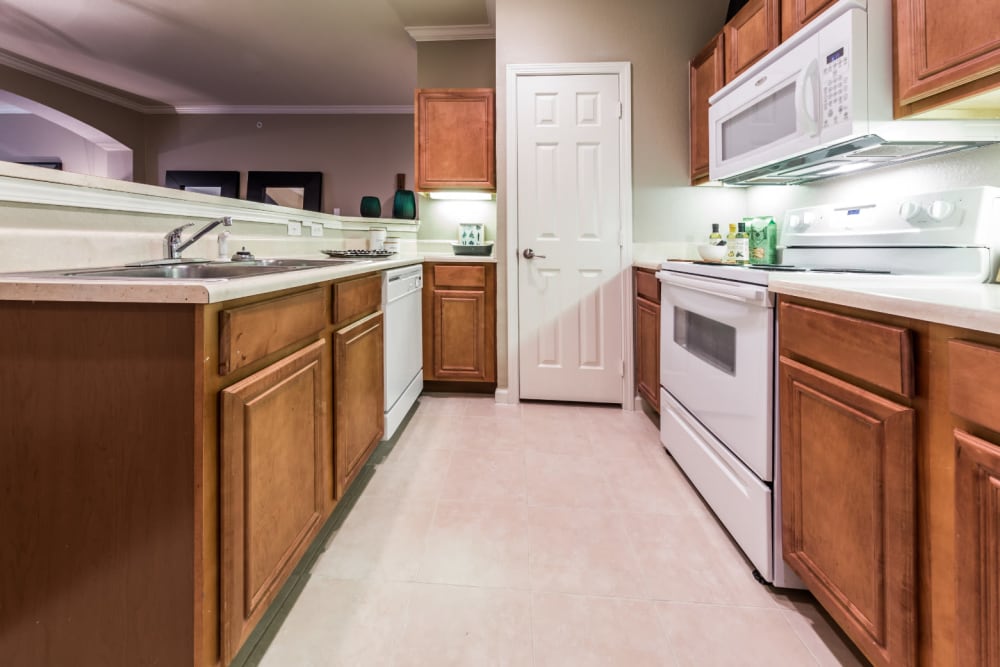 Bright kitchen with white appliances and wood cabinets and separate closed pantry at Marquis at The Cascades in Tyler, Texas
