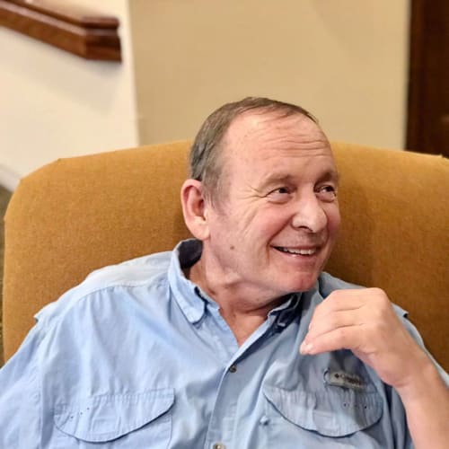 A seated resident smiling and looking off camera at Oxford Glen Memory Care at Carrollton in Carrollton, Texas