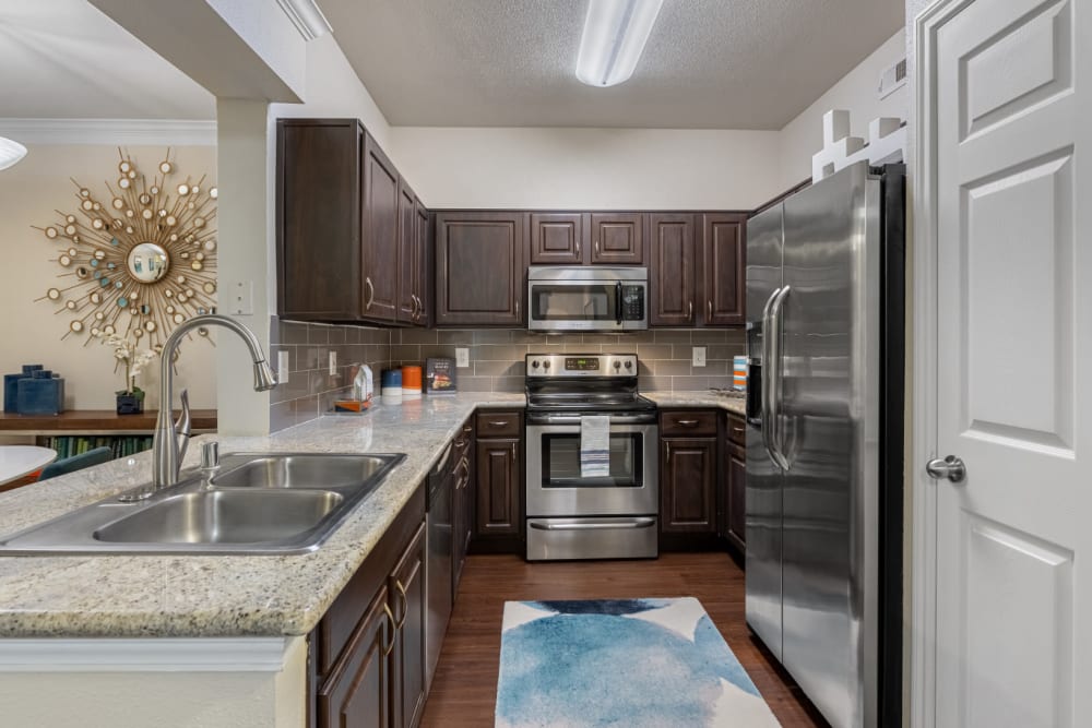Modern kitchen with granite counters, stainless steel appliances, and wood flooring at Marquis at Kingwood in Kingwood, Texas