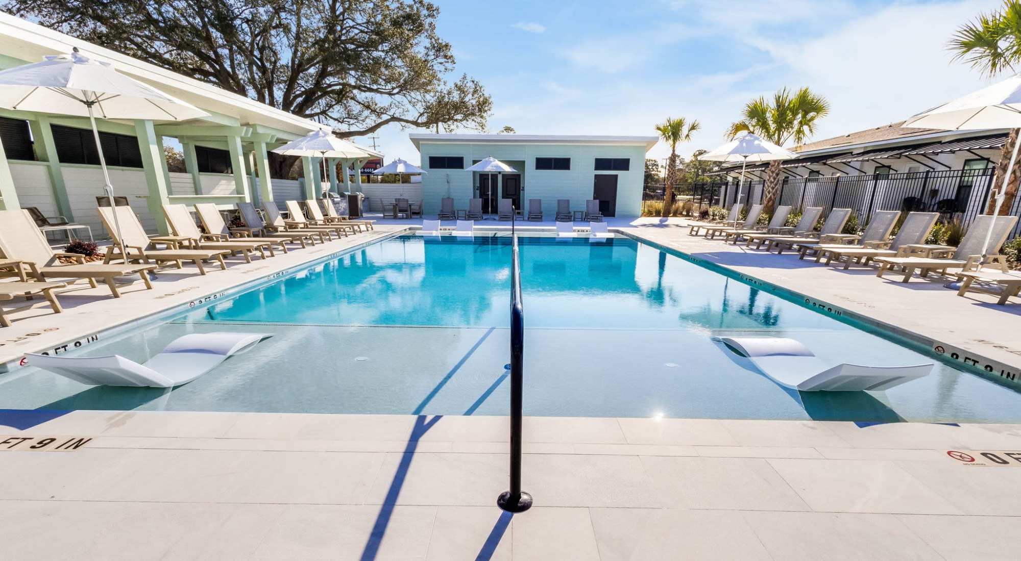Outdoor pool with clear blue water, surrounded by lounge chairs and white umbrellas at Amenities at Trinity Villas in Lafayette, Louisiana