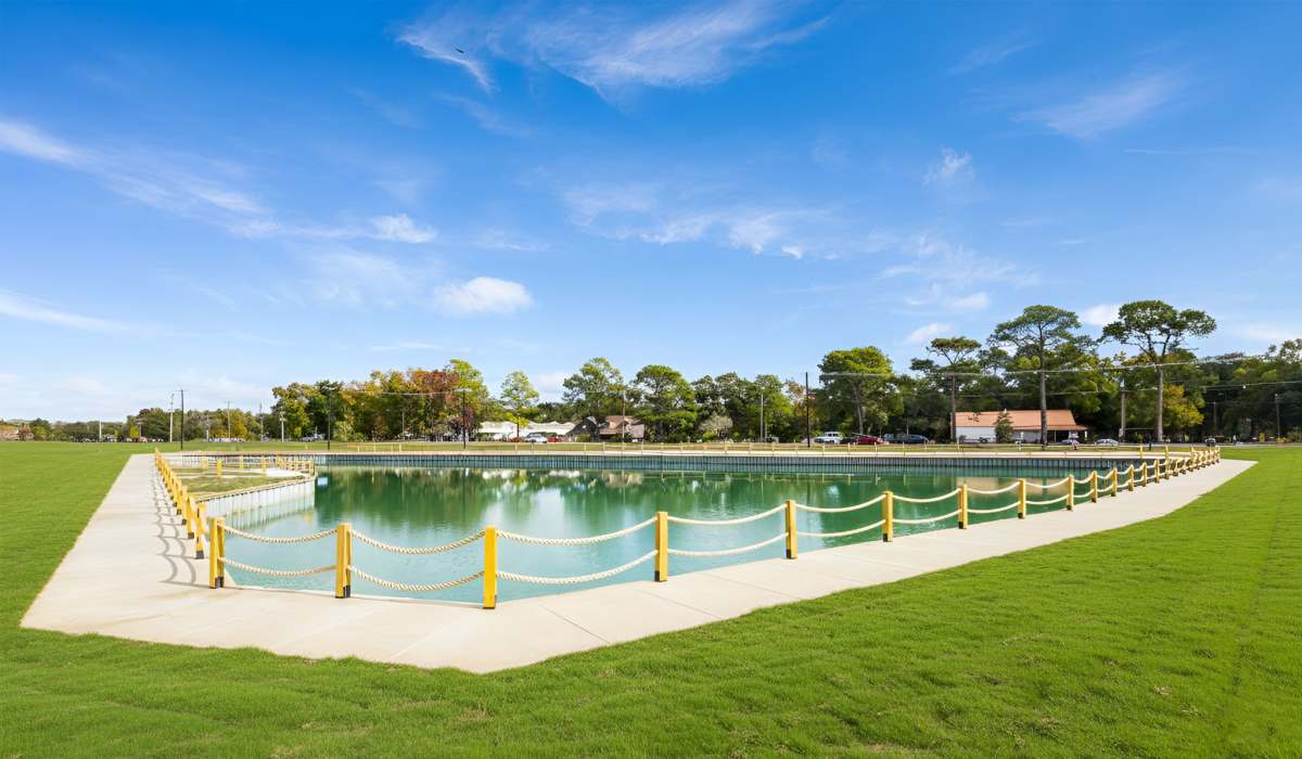 Sparkling water surrounded by green grass and a yellow rope fence under a clear blue sky at Lakewood Villas in Bossier City, Louisiana