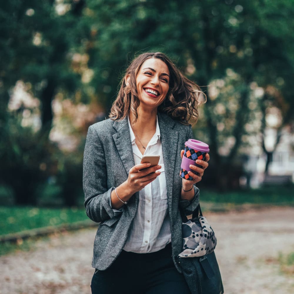 Resident laughing at something on her smartphone while walking to work with her morning coffee near Oaks Station Place in Minneapolis, Minnesota