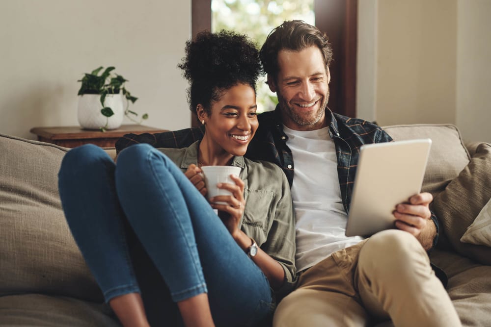 Happy residents browsing the web while relaxing on the couch with some coffee at Hilltops in Conroe, Texas