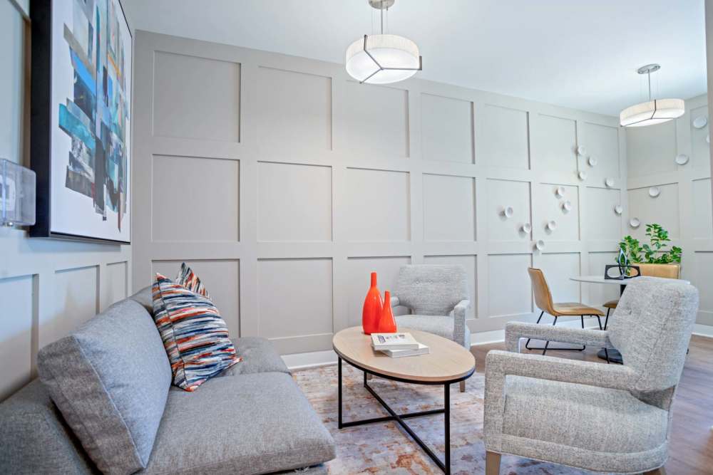 Modern lounge area with gray sofa, accent chairs, decorative artwork, and wooden flooring at Crestwood Manor in Frederick, Maryland