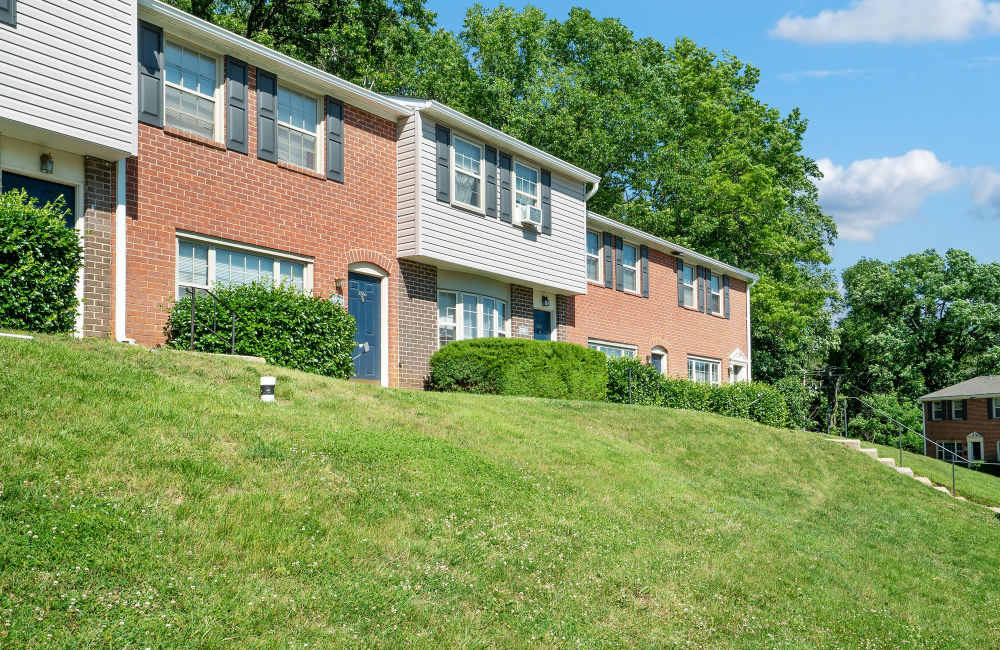 Two-story apartment buildings with green lawns and shrubs under a clear blue sky at Fairway Ridge in Baltimore, Maryland