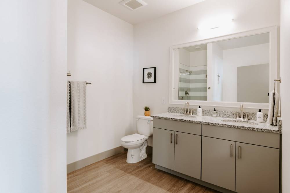 Modern bathroom featuring double vanity with granite countertops and stylish fixtures, wood-style flooring, and glass shower at Viña Apartments in Denver, Colorado