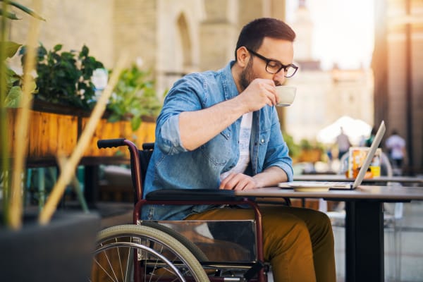 A gentleman in a wheelchair sipping coffee and looking at laptop at a nearby cafe at Elkhorn, Nebraska