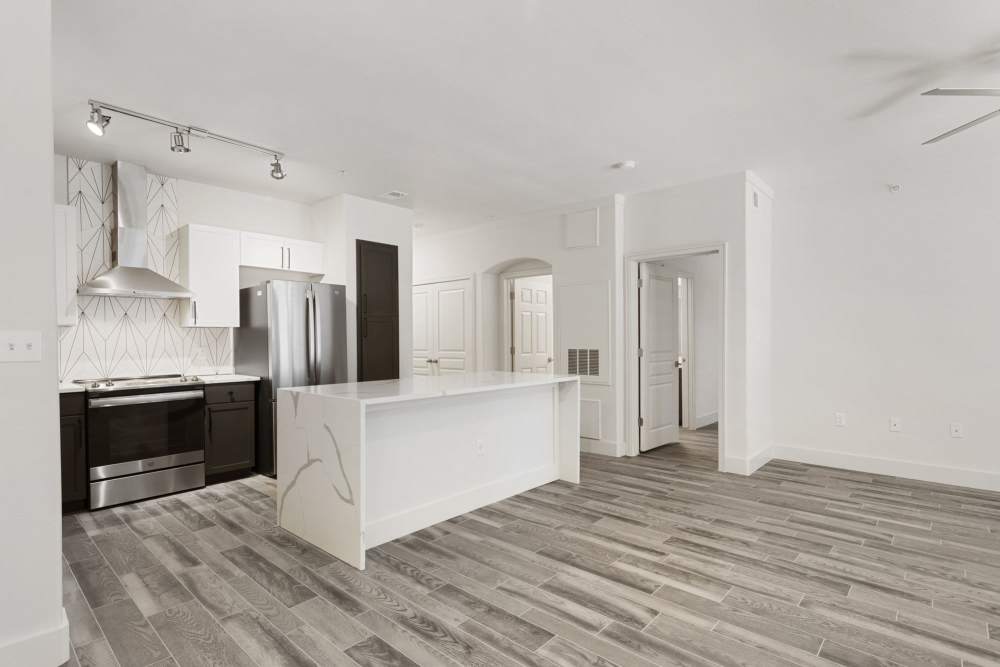 Open-layout kitchen and living room separated by island with waterfall faucet sink and dishwasher at The Berkeley in Fort Worth, Texas
