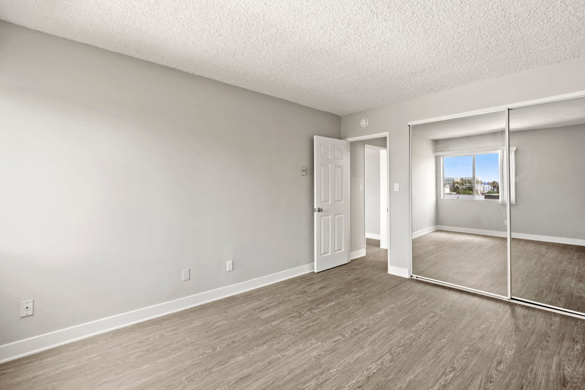 Bedroom with mirrored closet doors and wood-style flooring at Bay on 6th, Santa Monica, California