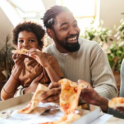Father and son enjoying pizza together at a dining table with natural light at Presidential Estates in Rochester, New York