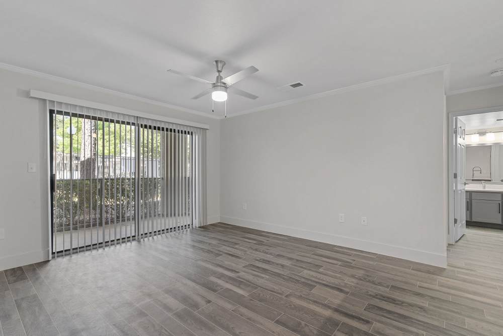 Wood-style floored living area with vertical blinds leading to the balcony at Seacrest in Katy, Texas