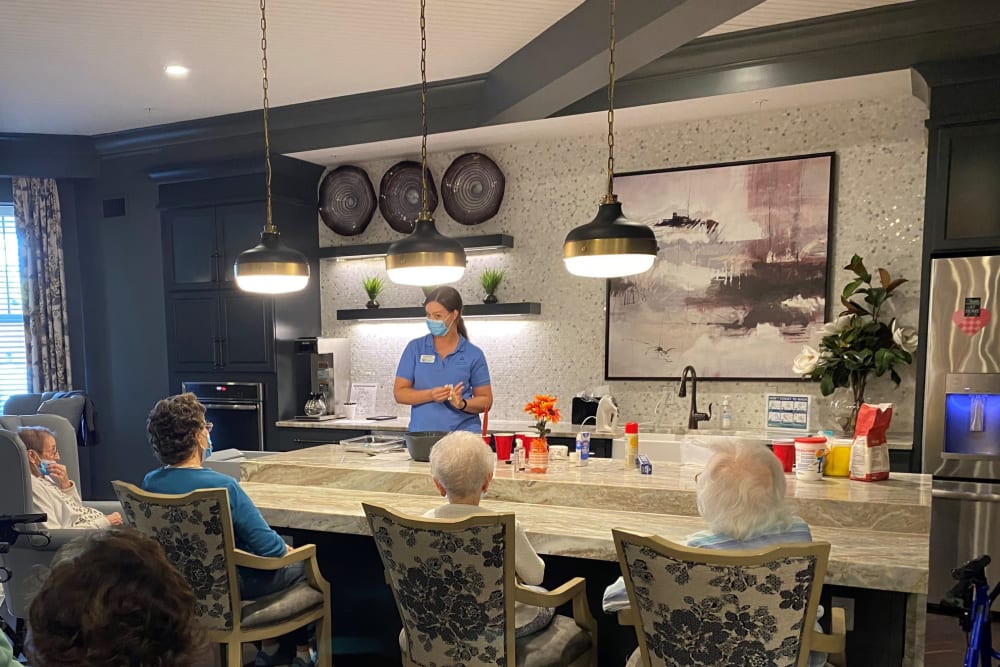 Masked nurse talking to a group of residents in a cafe at a Anthology Senior Living location